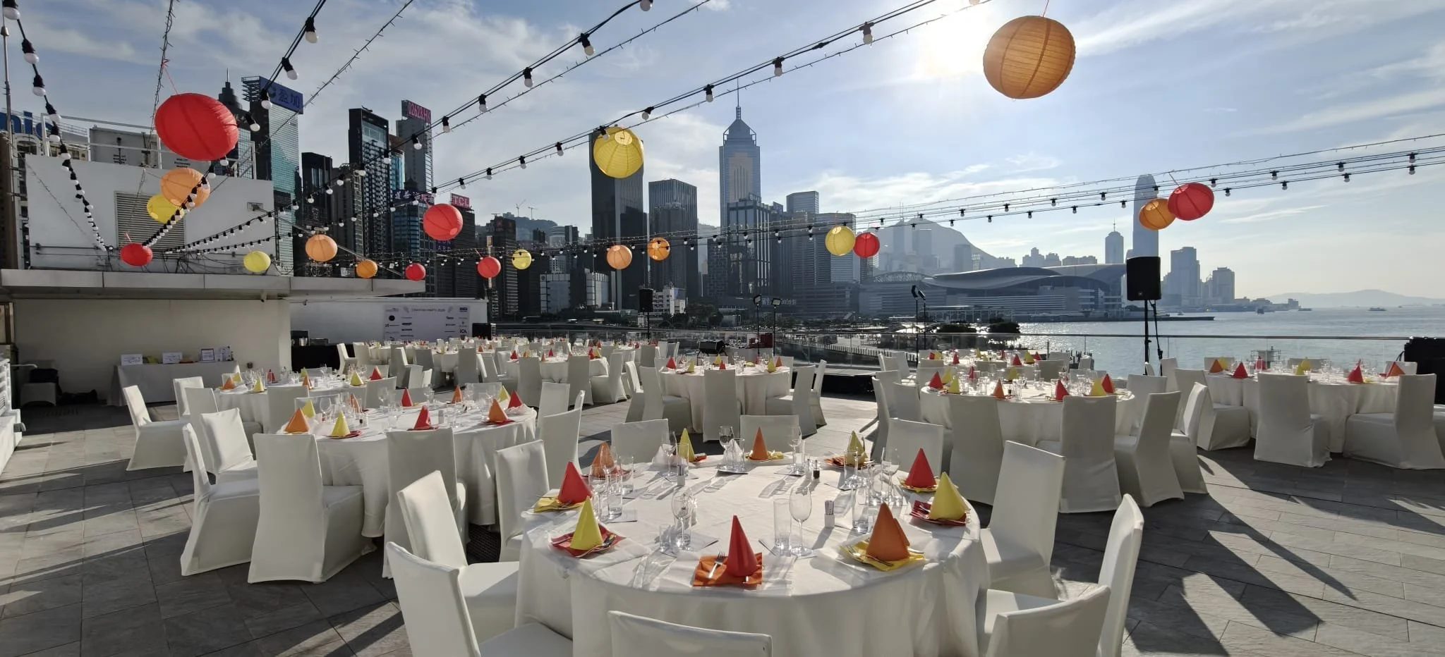 Tables laid for the Crayfish Party on the rooftop of the Royal Hong Kong Yacht Club, paper lanterns strung over the harbour and the Central skyline behind